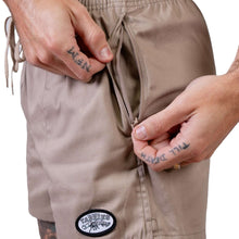 Load image into Gallery viewer, Close-up of hands opening zip pocket on khaki shorts, showcasing the functional design of Yabbies shorts for outdoor activities.